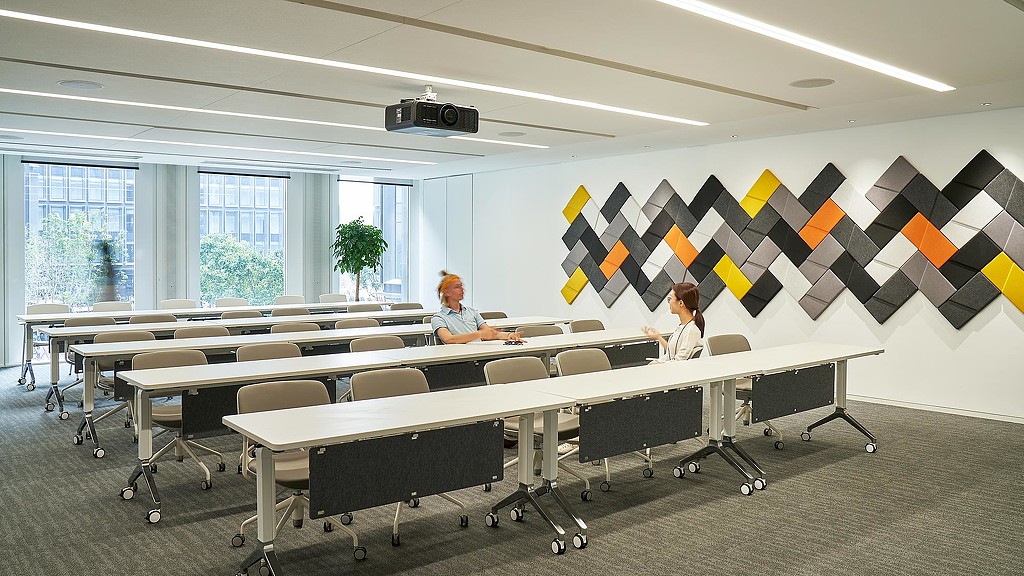 A couple of women sitting at a table with a projector screen.